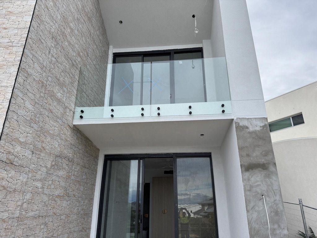 Frameless glass balcony balustrade on standoffs above a stone-clad entry