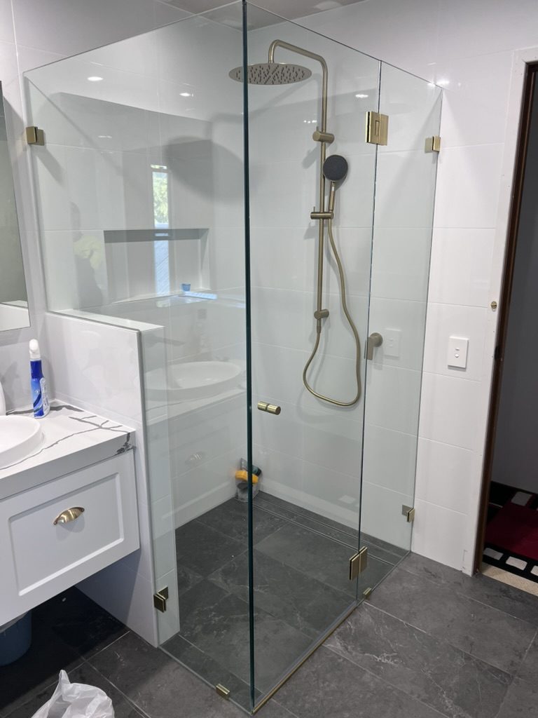 Frameless corner shower screen with brushed gold clamps