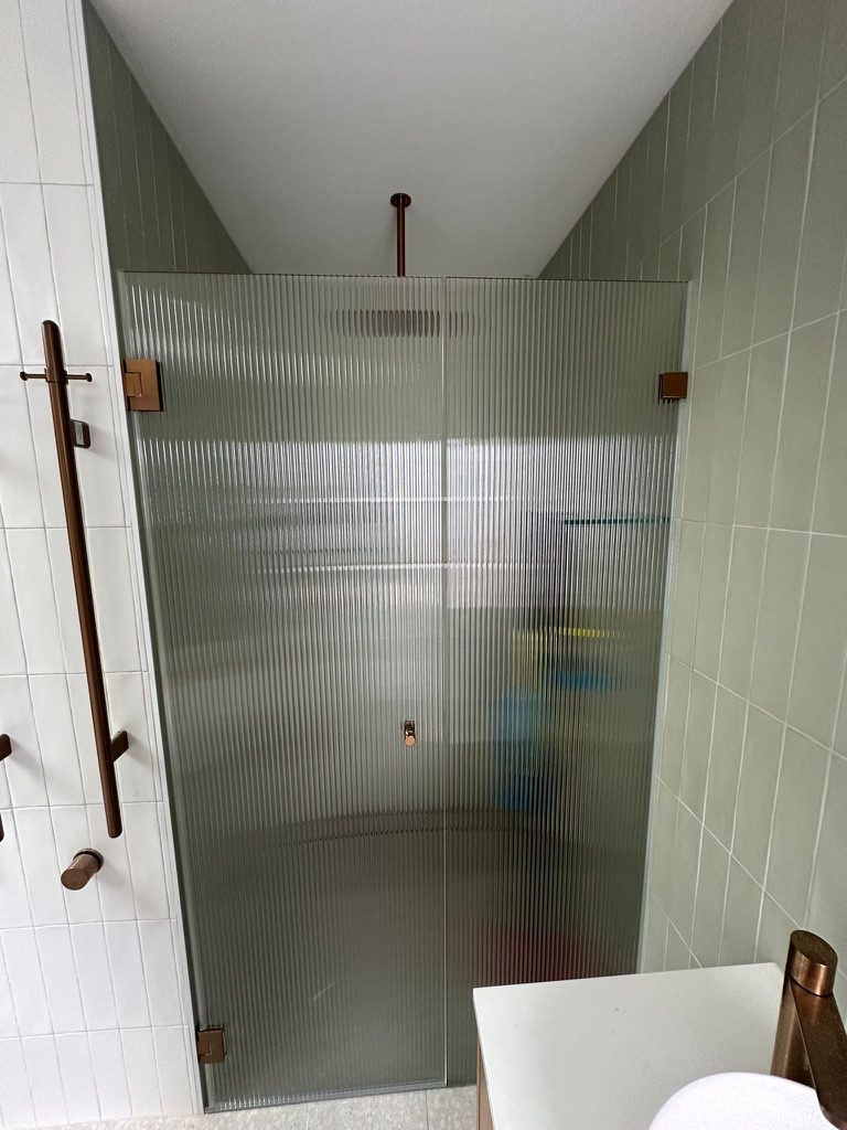 Frameless fluted glass shower door with brushed copper hardware
