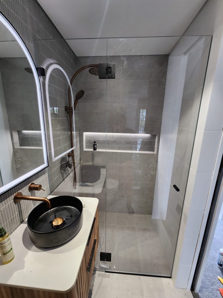 Frameless walk-in shower panel with matte black hardware and arched mirrors