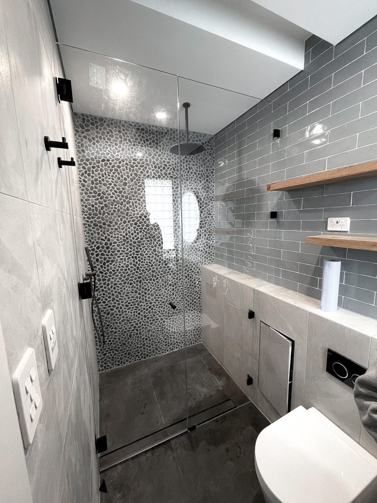 Frameless walk-in shower with matte black clamps and pebble feature wall