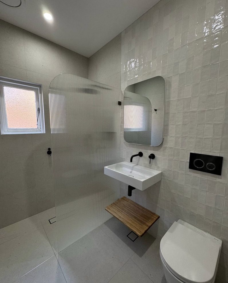 Frameless fluted glass walk-in shower divider with matte black tapware