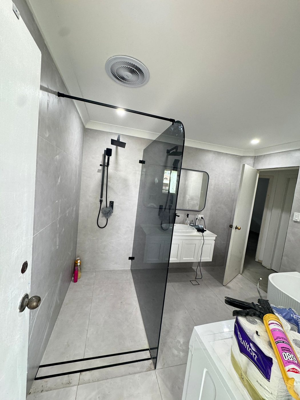 Smoked tinted frameless shower panel with grey concrete-look tiles