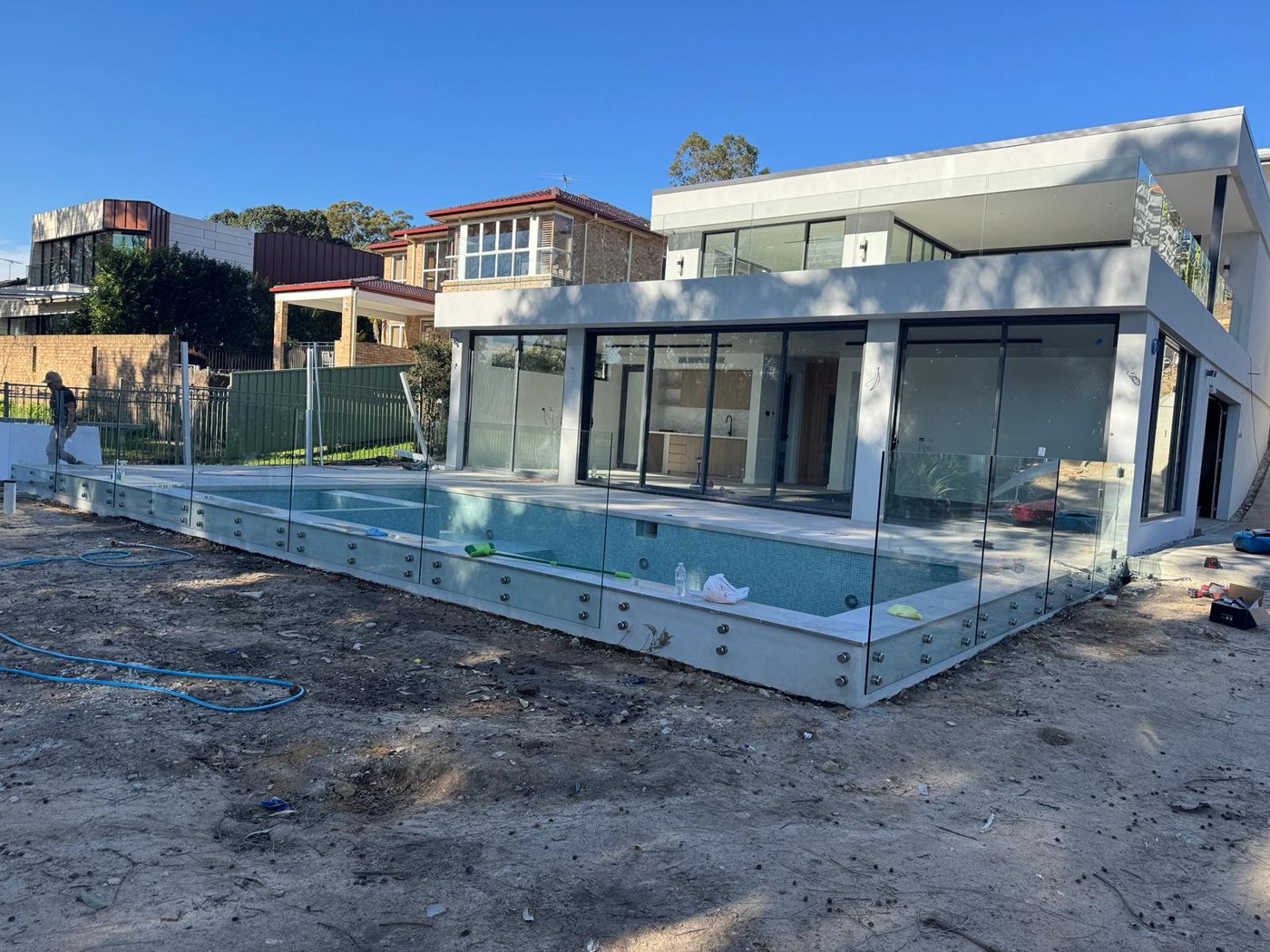 Frameless glass pool fence on a raised pool deck beside a modern home