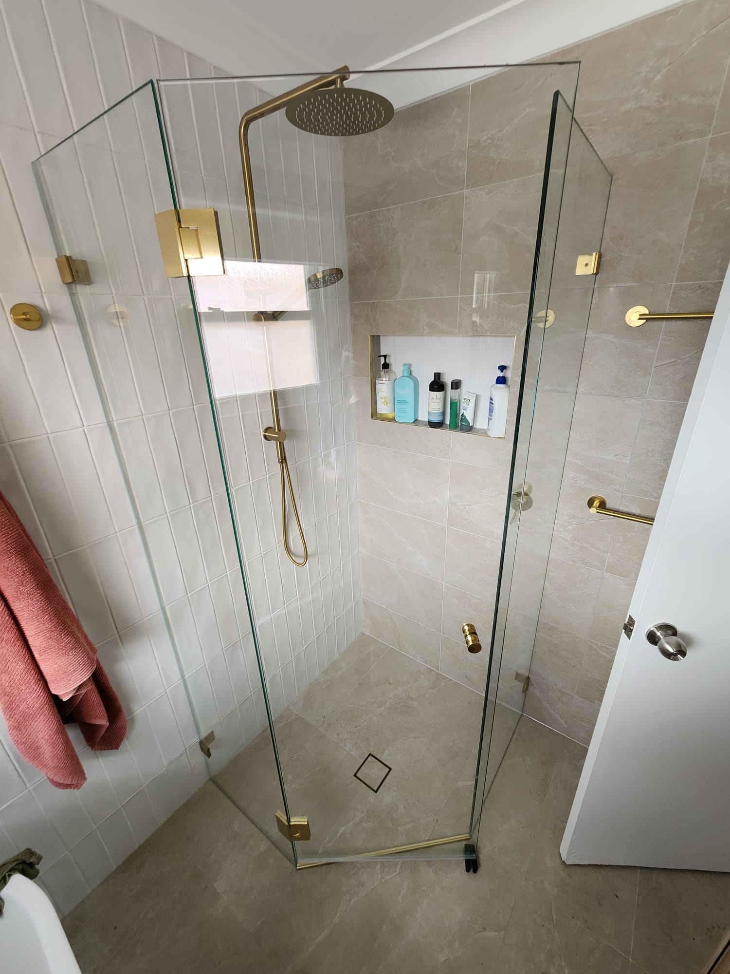 Frameless L-shape corner shower with matte black hardware over pebble tile