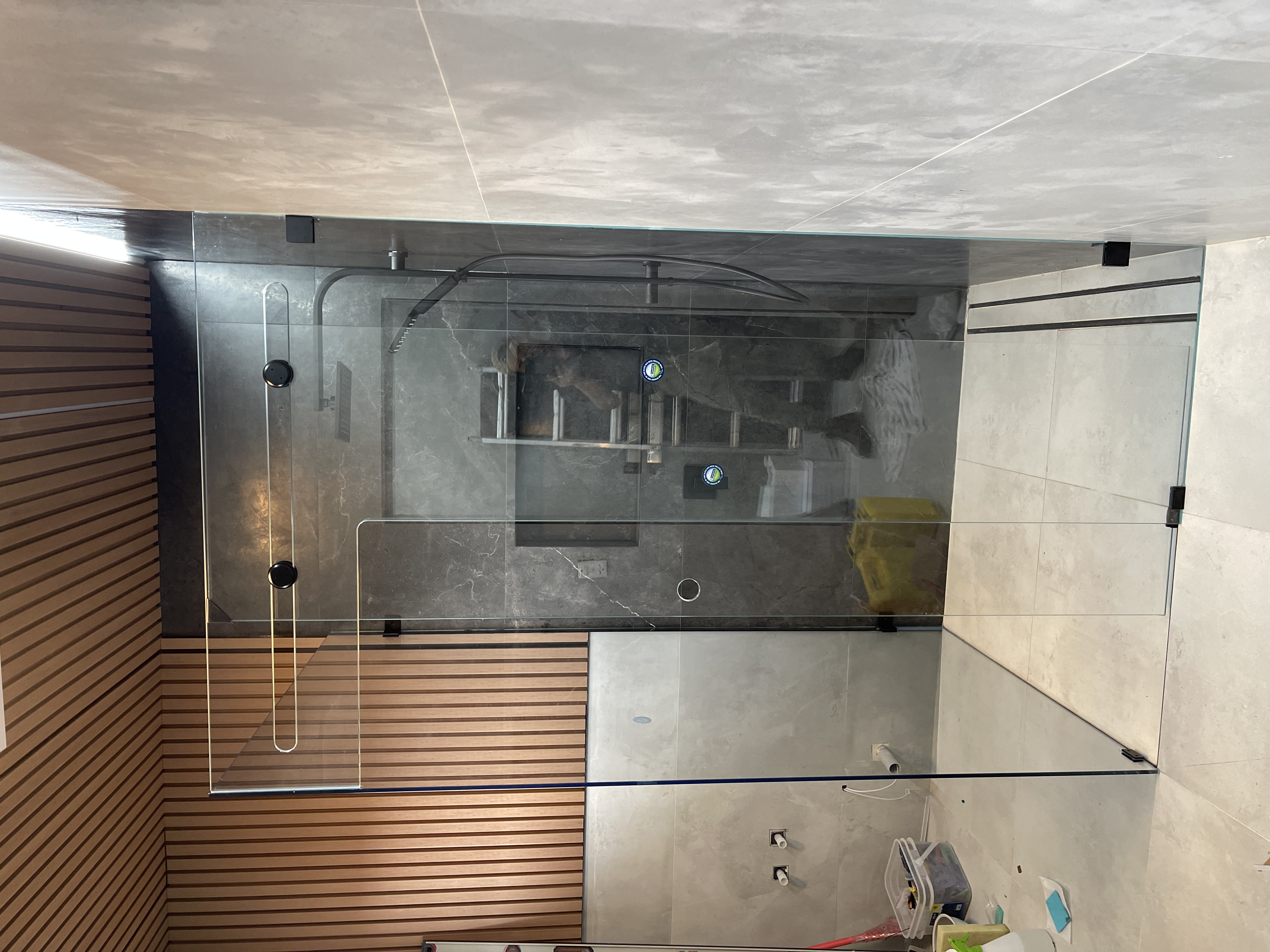 Frameless L-shape shower with matte black hardware under wood ceiling